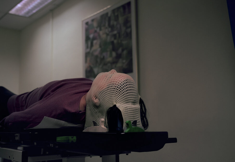 A person lies on a hospital be with their head covered in fabric awaiting a scan.