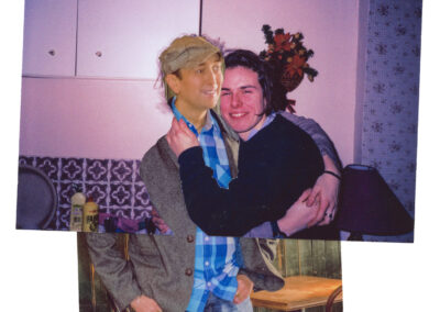 A collage-like image featuring two overlapping photographs. The top photo shows two people embracing warmly, with one person smiling widely while wearing a checkered shirt, jacket, and a cap. The background suggests a cozy, retro-style kitchen with floral tiles and cabinetry. The second person has their arm around the other, smiling with eyes slightly closed. The bottom photo is partially visible, showing the lower half of the person in jeans and a jacket, standing near a wooden table, hinting at a different setting. The layering creates a nostalgic, playful feel, blending two moments into one.